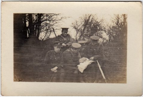 Photograph of a group of soldiers seated in countryside looking at papers