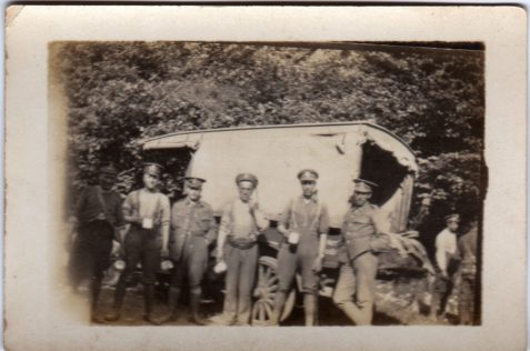 Photograph of six soldiers standing alongside a canvas-covered vehicle