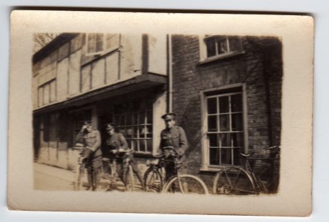 Photograph of three soldiers with bicycles outside a half-timbered building