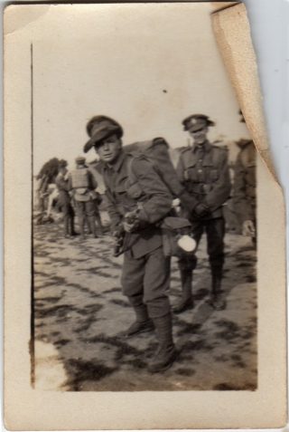 Photograph of a soldier pointing a rifle at the camera watched by two comrades