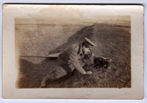 Photograph soldier crouched in a grassy trench with radio transmission equipment
