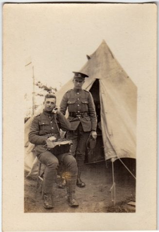 Photograph of two soldiers outside a tent, one standing, one seated with radio transmission equipment