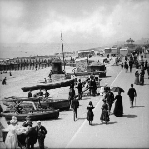 Promenaders along the Lower Esplanade, c. 1890: People promenading along the Lower Esplanade, west of the West Pier. Boats are on the beach, as are many bathing machines, one advertising 