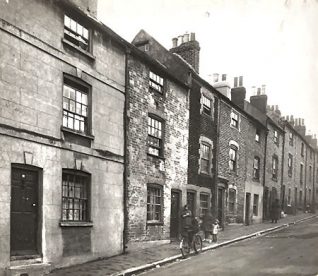 This is a photographic print of Richmond Hill, Brighton. It is a view northeast of several house fronts. Four pople can be seen standing in front of one of the doorways, while another figure is walking up the hill. A bicycle has been propped up against the kerb.  This photograph was commissioned by the Environmental Health department of Brighton Borough Council. It was intended to serve as part of a visual record of areas considered for slum clearance. Richmond Hill was demolished as part of the Morley Street redevelopment in the late 1930s. | Royal Pavilion and Museums Brighton and Hove