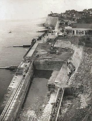 This photographic print was made by the Borough Surveyor's department in July 1932. It is a view west of Rottingdean seafront. Construction work on the Rottingdean bathing pool can be seen in the bottom half of the photograph.  The photograph was taken as part of a series recording work on improving sea defences in the area between Rottingdean and Saltdean. Designed by the Borough Engineer, David Edwards, these defences became part of the Undercliff Walk that runs east from Black Rock. | Reproduced courtesy of Royal Pavilion & Museums, Brighton & Hove