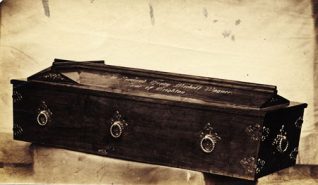 This photographic print shows the coffin of the Reverend Henry Wagner, Vicar of Brighton. The coffin bears an inscription and cross on the lid. It is situated on top of a stone plinth at an oblique angle.  Henry Wagner served as Vicar of Brighton from 1824 until his death in 1870. During this period he funded the construction of numerous churches in Brighton, such as St Paul's, West Street. Although his policies were occasionally controversial, he remained a popular cleric. His funeral procession in October 1870 was a major event: local churches were draped in black, and large crowds of people watched the coffin's journey to the Parochial Cemetery. This photograph was probably one of several taken to record the event. | Reproduced courtesy of Royal Pavilion and Museums Brighton and Hove