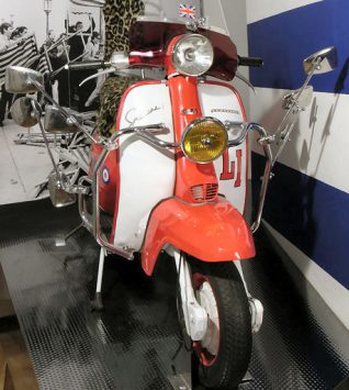 Lambretta Li 150 motor scooter, c1963, with a red and white livery steel body, which also features Union flag and classic mod target symbols. The seat is covered with an artificial leopard print fur cover. The scooter has extra outrider wing mirrors attached to the front and a Union flag is mounted on the aerial at the rear of the scooter. | Royal Pavilion & Museums, Brighton & Hove