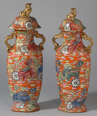 This pair of vases each have a fluted, oval body, narrow neck and a pair of gilded handles in the forms of fish. The lids are domed with a gilded knop in the form of a dog. Both the vase and its lid are decorated overall in enamel colours with a design of dogs holding stems of flowers in their mouths amidst swirling clouds, all against a bright orange ground. There are underglaze blue reign marks on the bases which may refer to the Qing Dynasty emperor Jiaqing. | Reproduced courtesy of Royal Pavilion, & Museums, Brighton & Hove