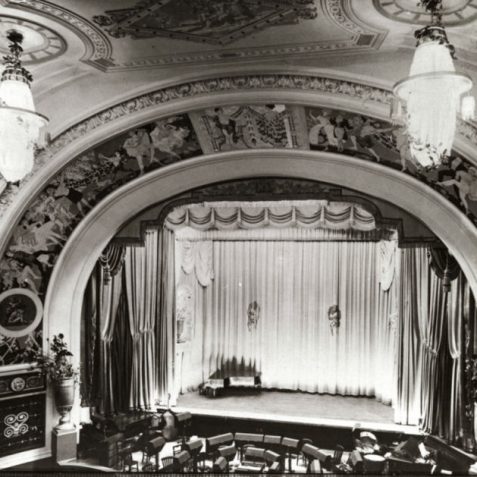 A view of the centre stage with the orchestra pit visible at the bottom of the picture. The photograph is focused on the theatre's Proscenium Arch. This was painted by Lawrence Preston of the Brighton School of Art, and features a number of dancing figures. | Image reproduced with kind permission of The Royal Pavilion and Museums Brighton and Hove