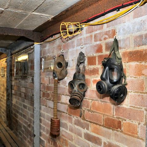 Gas masks from the 1940s (the one on the right is contemporary) and the bench seating that was throughout the shelter | Photo by Tony Mould