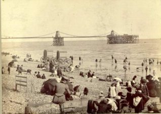 Bathing Machines near Chain Pier, c. 1890: Children paddling in the sea, watched by their families from the beach. Two bathing machines at the water's edge. | Image reproduced with kind permission from Brighton and Hove in Pictures by Brighton and Hove City Council