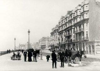 King's Road and Queen's Hotel, c. 1890: King's Road c. 1890 looking west past Queen's hotel. In foreground is a horse cab, railings, seats and street lights are prominent. | Image reproduced with kind permission from Brighton and Hove in Pictures by Brighton and Hove City Council