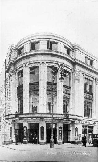 Corner Side Entrance of Savoy Cinema, 1930: The Savoy Cinema opened on 1 August 1930 on the site of Brill's Baths in Pool Valley. Two uniformed doormen can be seen at the doors of the corner entrance in East Street to the cinema. From 1963 it has been known as the ABC cinema. In 1975-76 the cinema was converted into 4 smaller screens, the largest of which has been disused for several years. In 1999-2000 the cinema was due to be converted into a casino, bar and restaurant development. | Image reproduced with kind permission from Brighton and Hove in Pictures by Brighton and Hove City Council