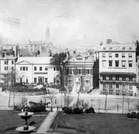 Buildings on West Side of the Old Steine, c. 1890: Marlborough House built in 1765 is the oldest remaining house on the Steine, and gained its name when owned by the fourth Duke of Marlborough between 1771 and 1786. In this photograph it was then the Brighton Board School Office. Steine House, built in 1804 for Maria Fitzherbert, is now a YMCA hostel. Blenheim House was then The Albany School for Girls. Victoria Fountain, supported by three entwined dolphins on a base of sarsen stones was installed at the centre of the Steine by Amon Henry Wilds in 1846 | Image reproduced with kind permission from Brighton and Hove in Pictures by Brighton and Hove City Council