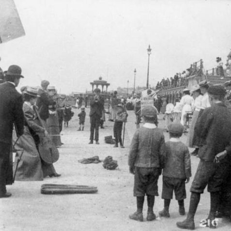 Musicians on Brighton Beach, 1899: A small orchestra performing on the Lower Esplanade. Behind them is the King's Road Bandstand. On the right a cart advertises J. Walski's Nougat. | Image reproduced with kind permission from Brighton and Hove in Pictures by Brighton and Hove City Council
