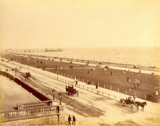 Brunswick Lawns, c. 1905: Brunswick Lawns looking east from the entrance to Adelaide Crescent towards the West Pier. People are promenading along the lawns while horse-drawn carriages travel along Kingsway. | Image reproduced with kind permission from Brighton and Hove in Pictures by Brighton and Hove City Council